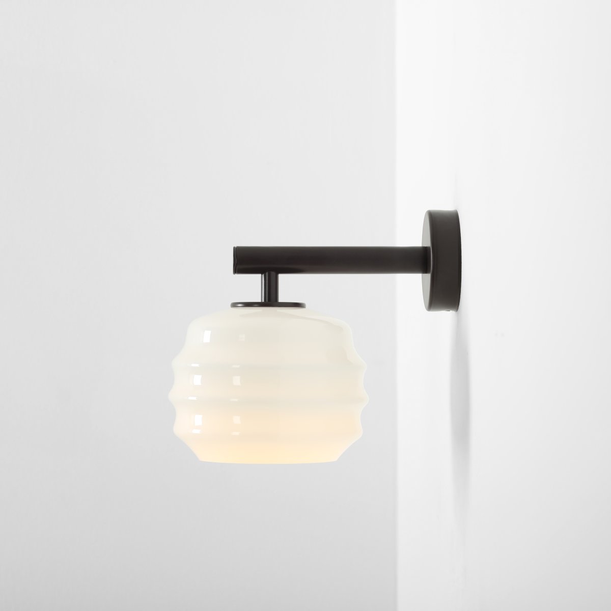 Puff 23cm brun foncé applique murale De Artera - Son abat-jour décoratif en verre opale blanc séduit par sa forme incurvée, conférant à la lampe une allure à la fois ludique et raffinée.