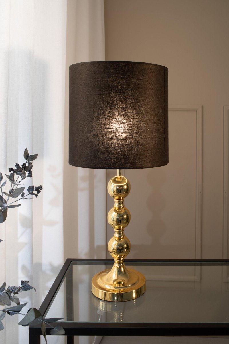 Octo 57cm Laiton lampe de table De Markslöjd - Octo est une &eacute;l&eacute;gante lampe de table avec un abat-jour en lin noir et une base de lampe couleur laiton en forme de trois sph&egrave;res douces et rondes.