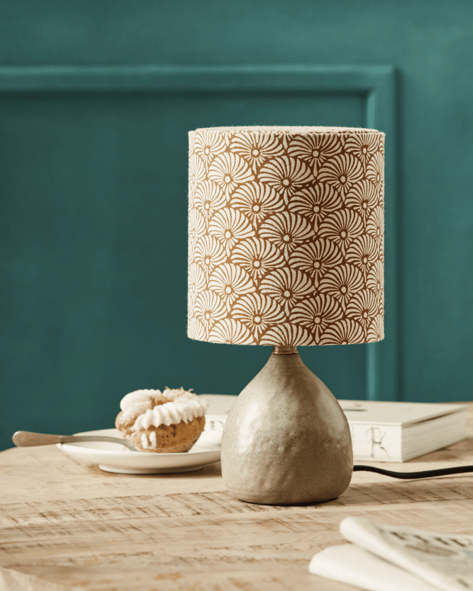 Flores 30cm Sable lampe de table De House Doctor - Il est doté d'une base en céramique couleur sable et d'un abat-jour en lin décoré de motifs de plumes de soleil sable et marron imprimés à la main, équilibrant magnifiquement une esthétique moderne et chaleureuse.