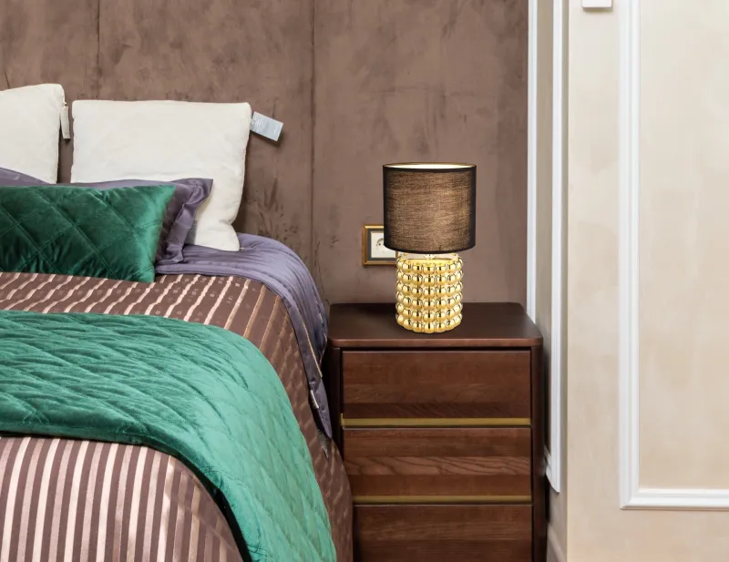 Valentino 33cm Or lampe de table De Globo Lighting - P&aring; en cylinderformad fot i guldf&auml;rgad keramik vilar en stilren, svart textilsk&auml;rm.