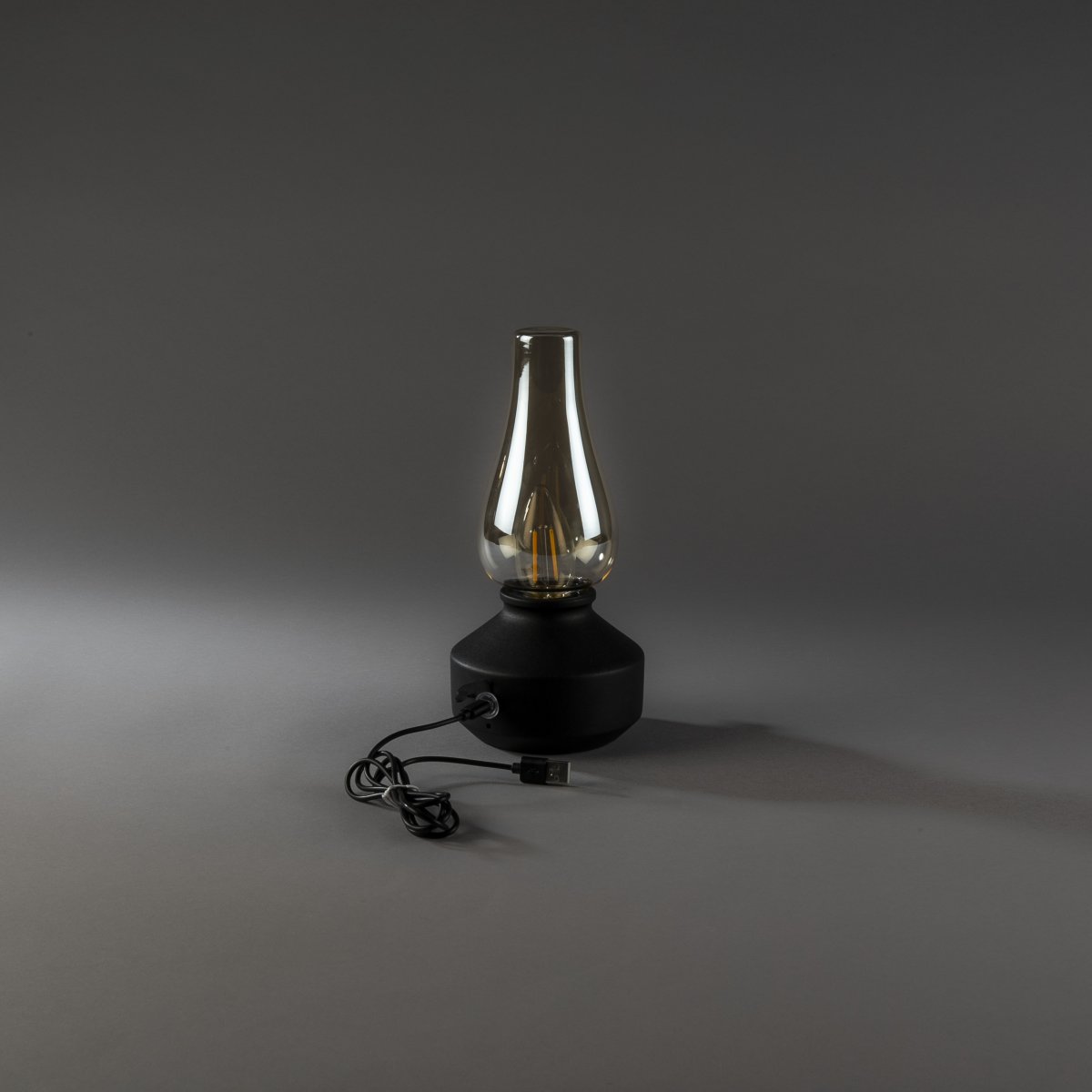 Lampe de table rechargeable 25cm Noir portable De Konstsmide - Fabriquée en métal et en verre, elle est dotée d'un socle noir et d'un variateur pratique permettant de régler facilement l'intensité de sa lumière blanche chaude et tamisée.