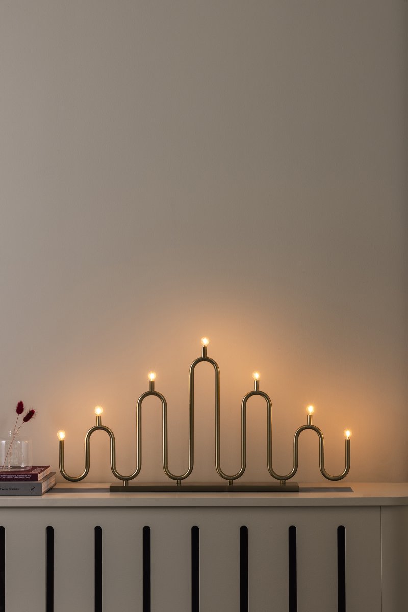 Noel 7 Laiton De Globen Lighting - Son design aux courbes douces, obtenu par le cintrage à la main de tubes métalliques, offre une interprétation moderne du bougeoir classique de l'Avent.