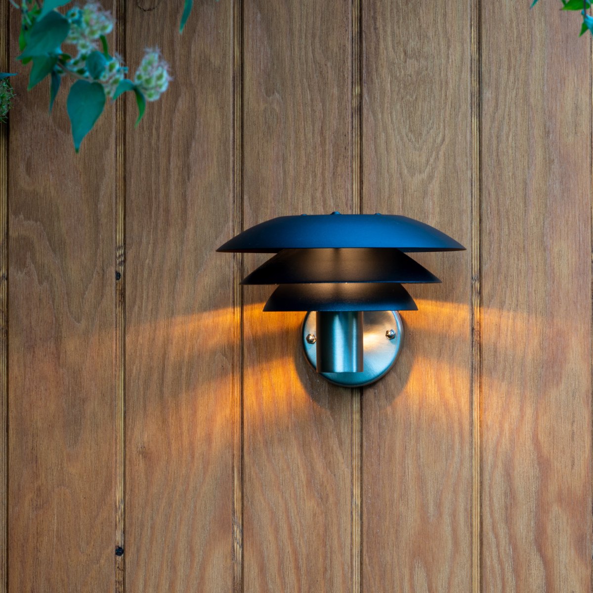 DL20 Acier inoxydable lampe d’extérieur De Dyberg Larsen - La lampe est dotée de trois abat-jour emblématiques de différentes tailles qui diffusent une lumière magique et est fabriquée en acier inoxydable avec d'élégants abat-jour noirs mats.