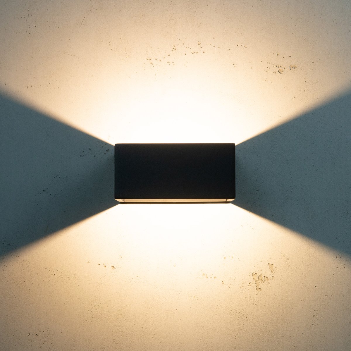 Jupiter Noir lampe d’extérieur De Dyberg Larsen - Jupiter a un côté plat sur le mur et une face avant semi-circulaire avec une source de lumière LED qui brille de haut en bas le long du mur.