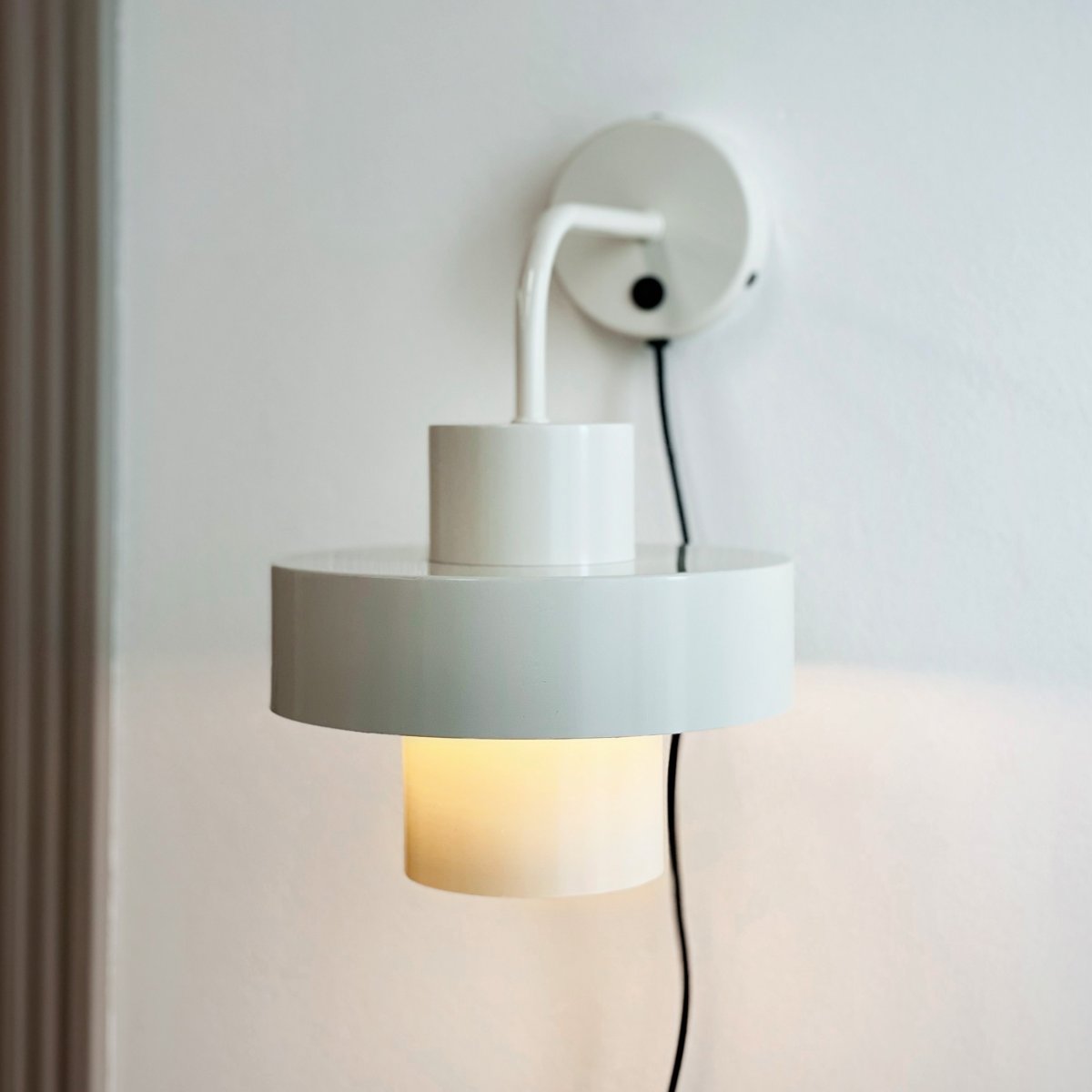 Stoke Ø15 Blanc applique murale De Dyberg Larsen - Il est fabriqué en métal avec une surface brillante qui met en valeur les formes cylindriques de la lampe et crée un contraste équilibré avec d'autres matériaux tels que la pierre, le bois et le verre.