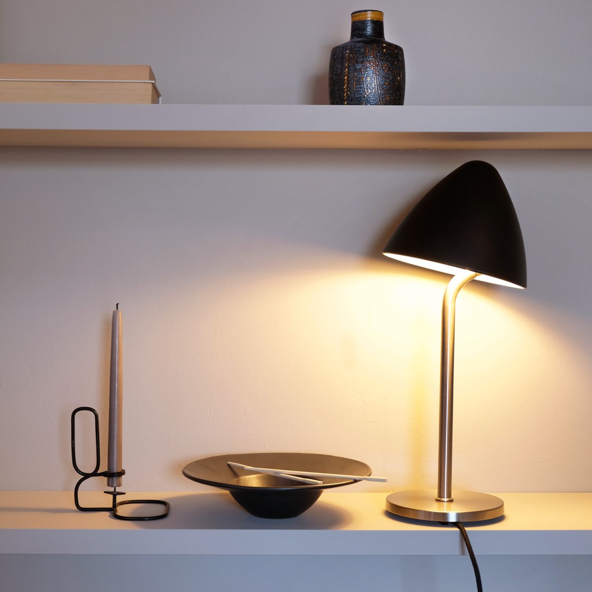 Oulu 47cm Noir lampe de table De Dyberg Larsen - La lampe ajoute une touche moderne et élégante à votre maison, avec le contraste entre la couleur noire profonde et l'acier brossé créant une expression intemporelle.