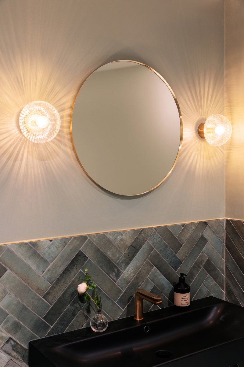 Fungo Ø16 Laiton transparent/brossé lampe de salle de bain De Globen Lighting - Son abat-jour en verre soufflé à la main, à la texture nervurée et aux bulles d'air, crée un magnifique jeu de lumière dans la pièce.