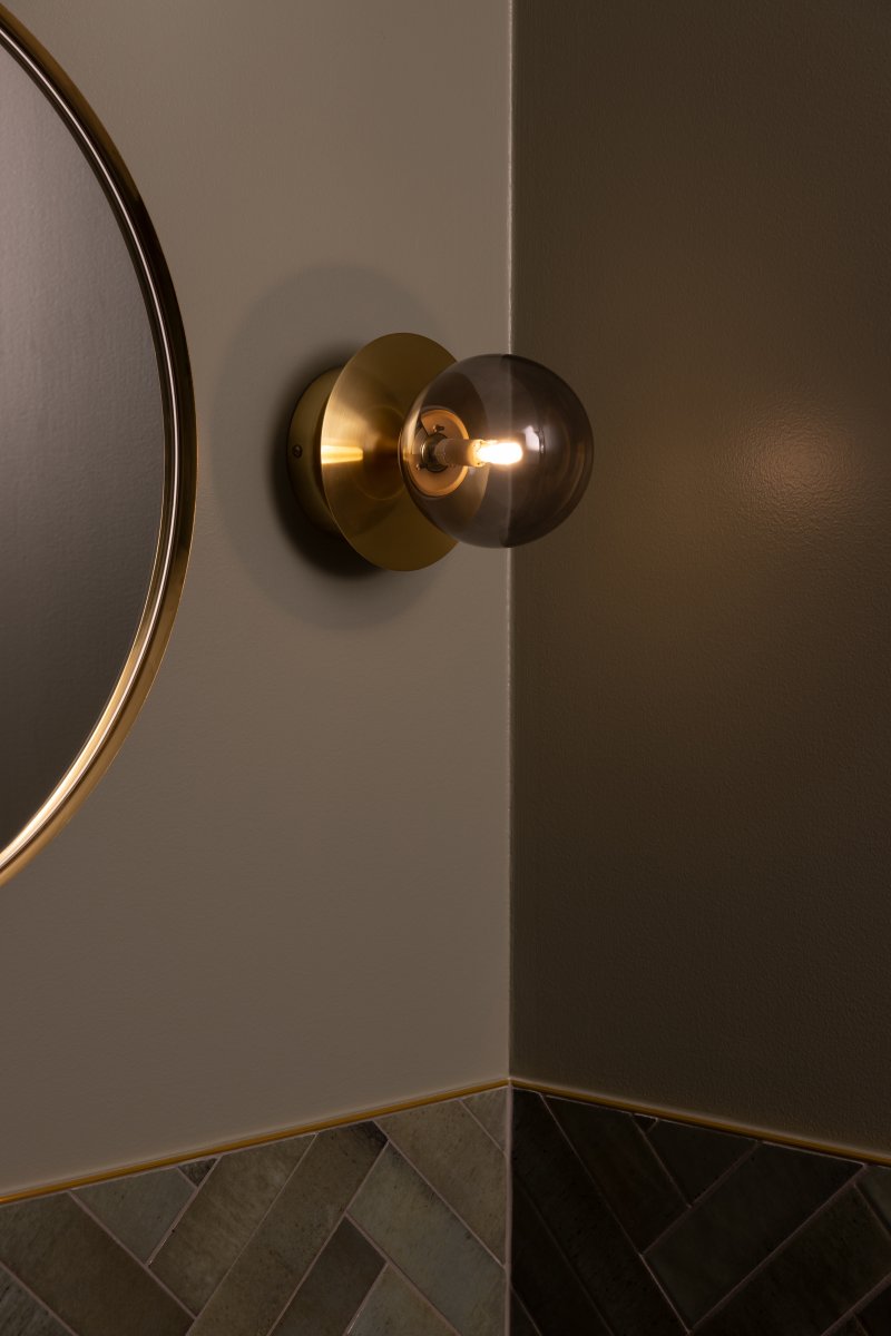 Art Deco Ø16 Laiton brossé/fumé lampe de salle de bain De Globen Lighting - Fabriqué en métal, il est doté d'un abat-jour en verre fumé qui diffuse une lumière éclatante dans la pièce.