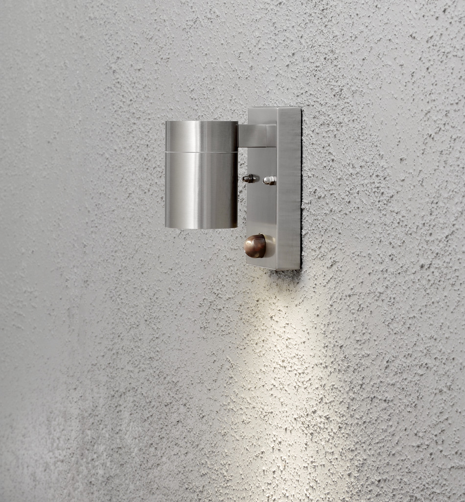 Modena Argent lampe d’extérieur De Konstsmide - Le design élégant et moderne de la lampe s'intègre dans n'importe quelle façade et s'allume automatiquement lorsqu'elle détecte un mouvement, offrant une sécurité supplémentaire dans les entrées et les allées.