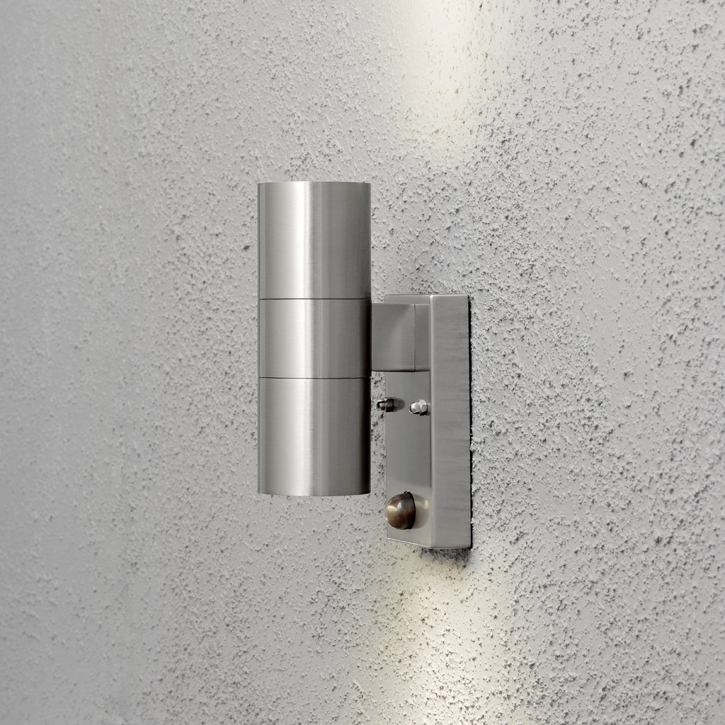 Modena Argent lampe d’extérieur De Konstsmide - Le design élégant et moderne de la lampe s'intègre dans n'importe quelle façade et s'allume automatiquement lorsqu'elle détecte un mouvement, offrant une sécurité supplémentaire dans les entrées et les allées.