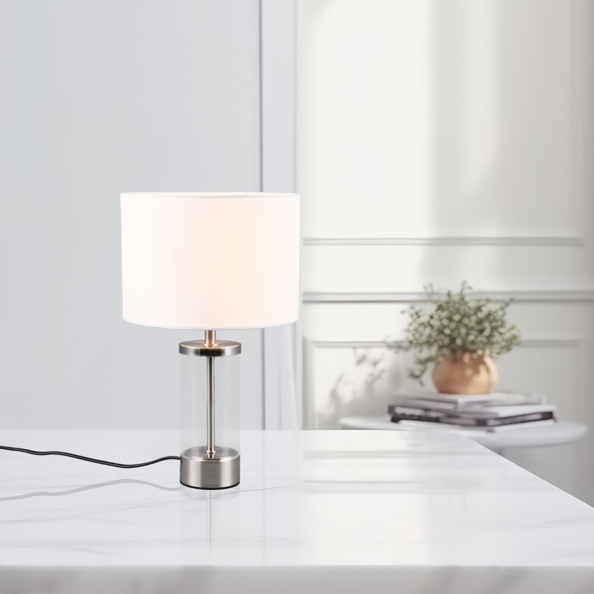 Grazia 34cm Blanc lampe de table De Trio Lighting - La lampe de table Grazia combine un élégant abat-jour en tissu avec une base cylindrique élégante en verre et en métal, créant une impression harmonieuse et élégante.