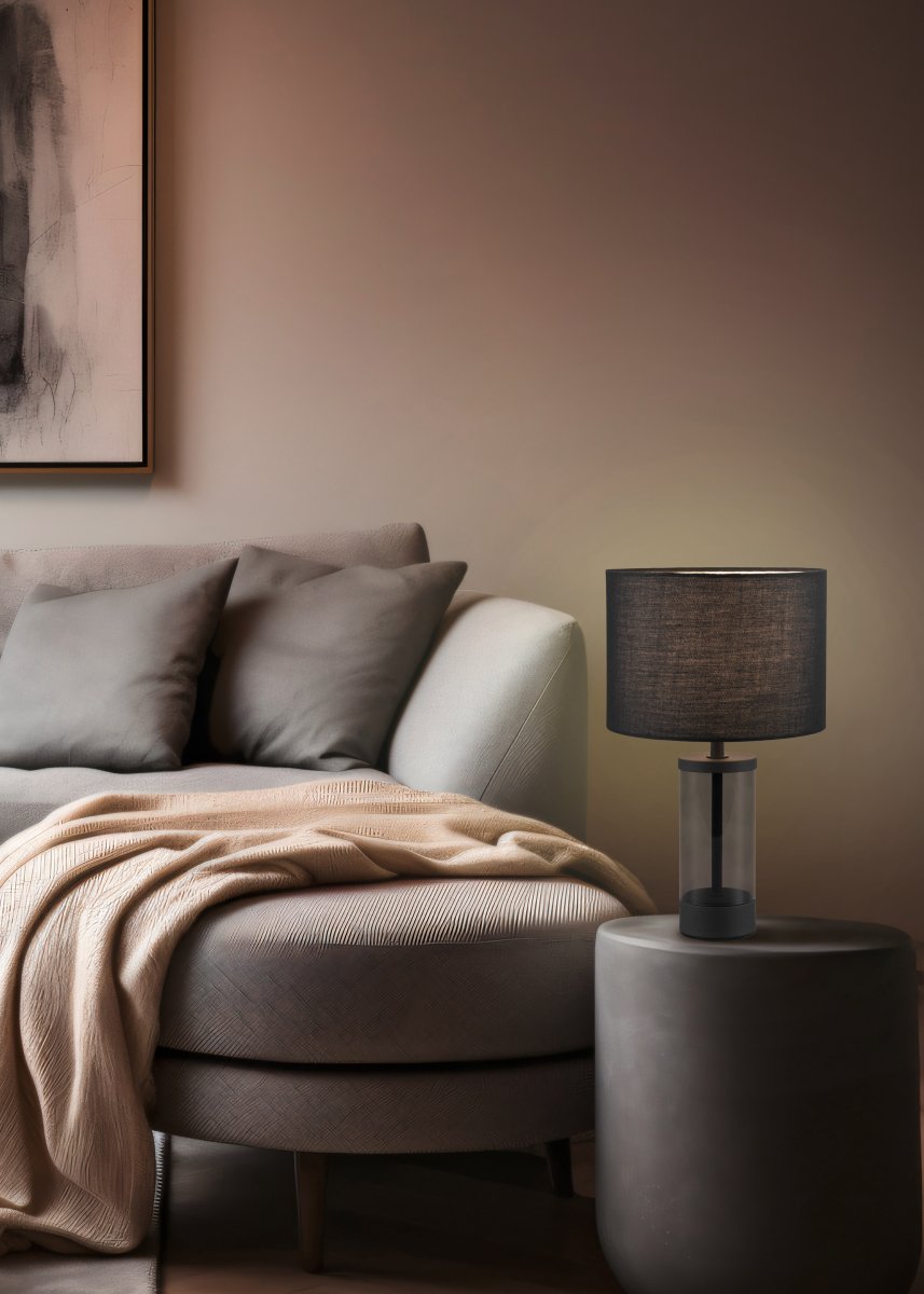 Grazia 34cm Noir lampe de table De Trio Lighting - La lampe de table Grazia combine un élégant abat-jour en tissu avec une base cylindrique élégante en verre et en métal, créant une impression harmonieuse et élégante.